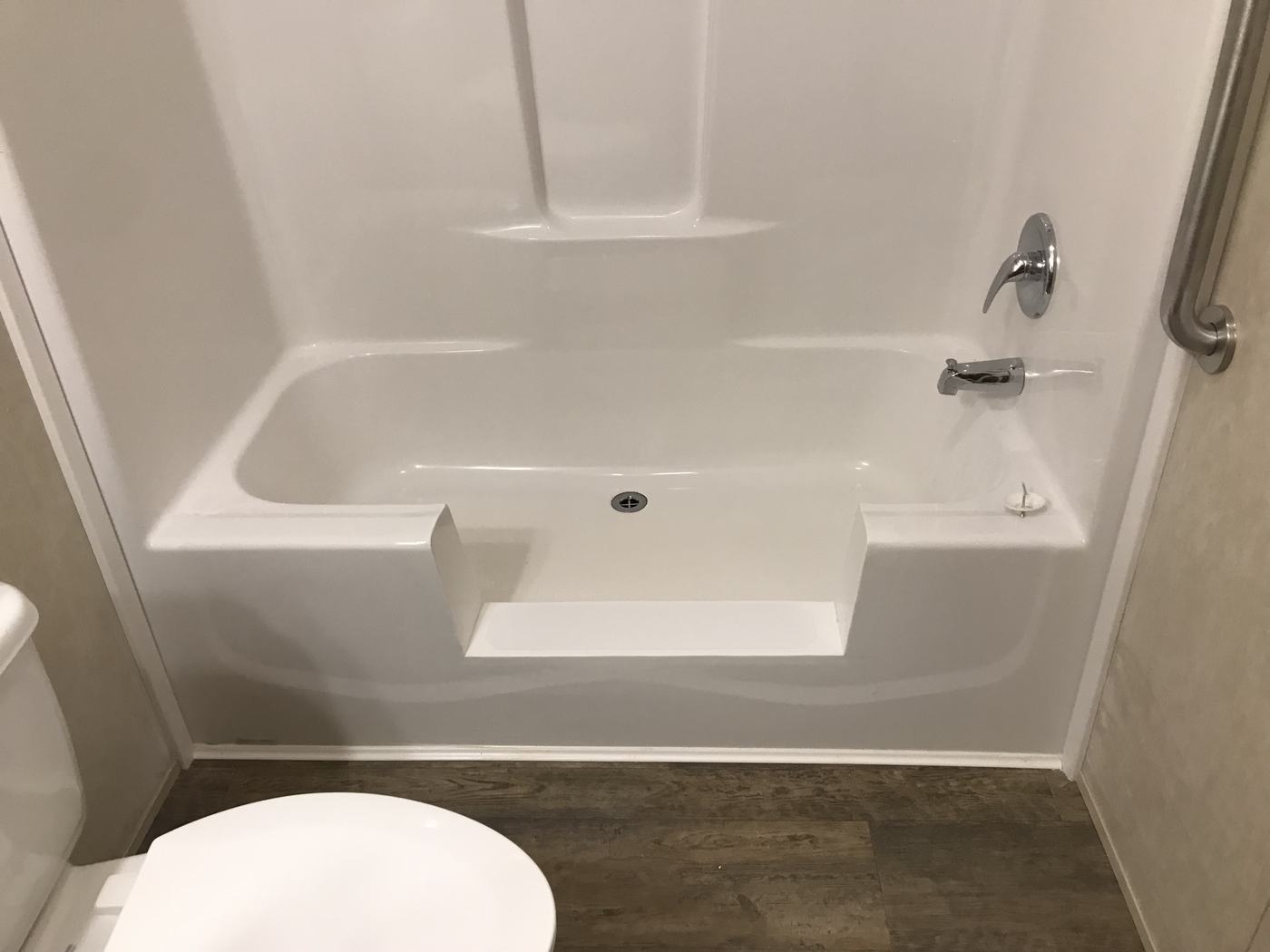 A completed TubcuT conversion — the existing tub left intact with a step-through opening cut into the side, beside a wall-mounted grab bar