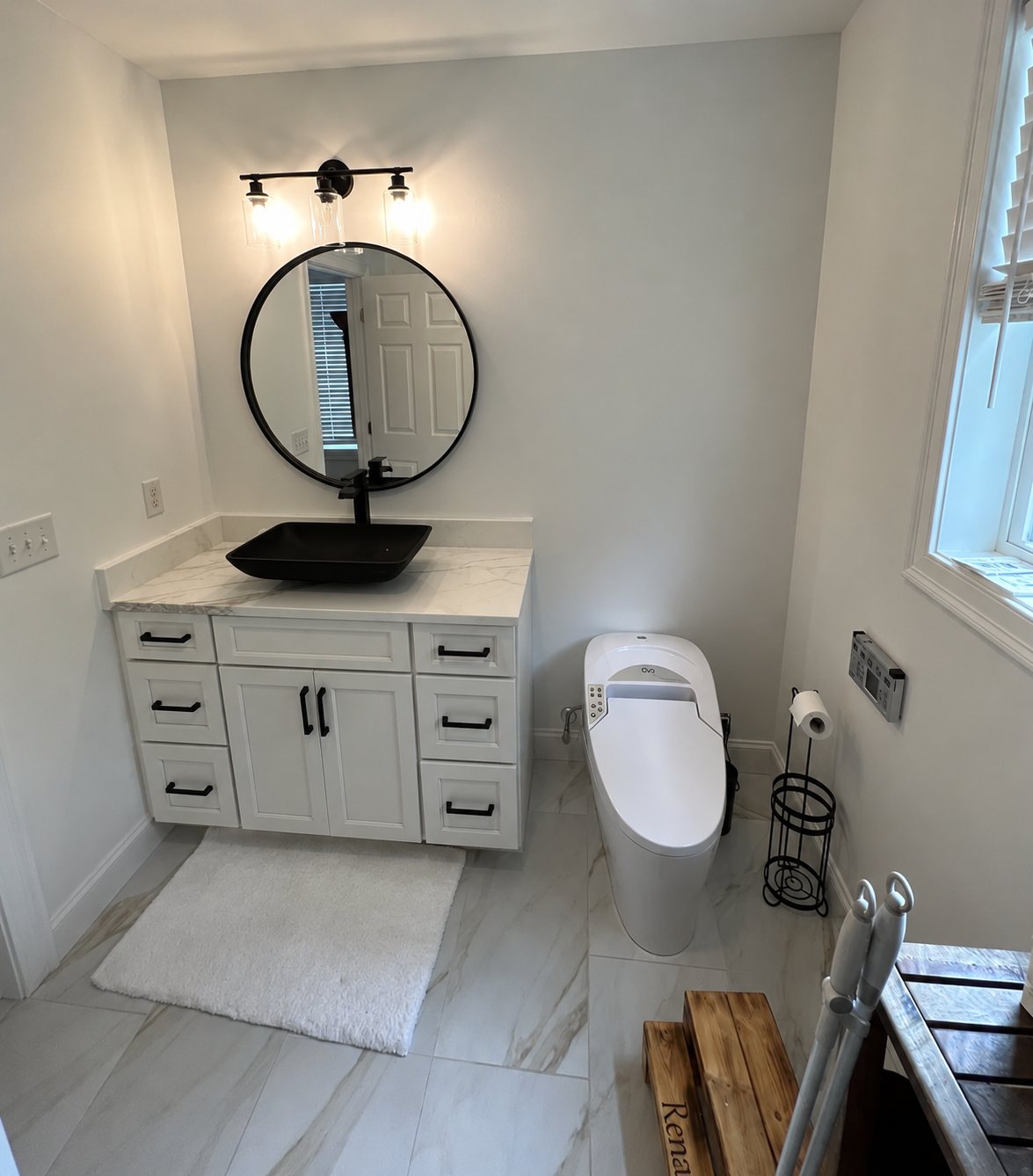Restored bathroom with new vanity, round mirror and marble tile